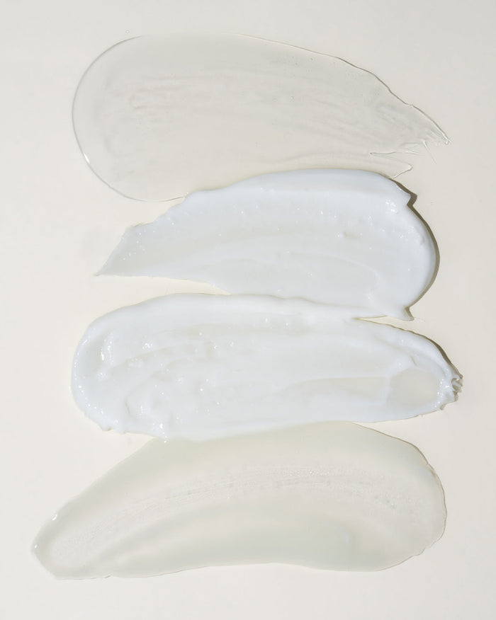 Three smears of white cream on a light gray background