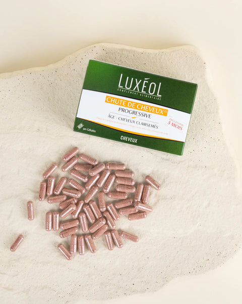 Luxéol juuksevärvi toote pakend roosade kapslitega beežil kangast taustal