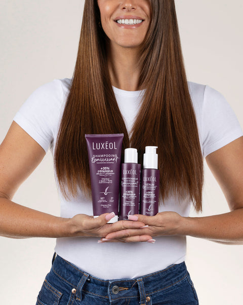 Woman holding Luxéol hair care products against a plain background